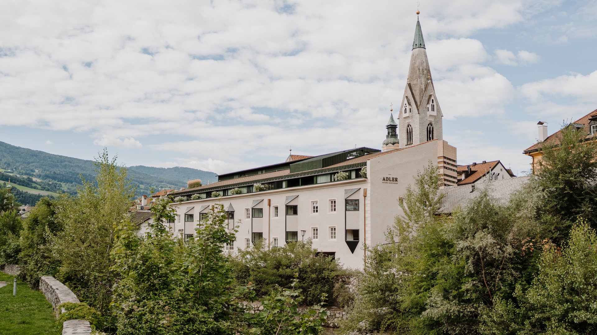 Kirchturm über historischen Gebäuden und grüner Landschaft mit Fluss