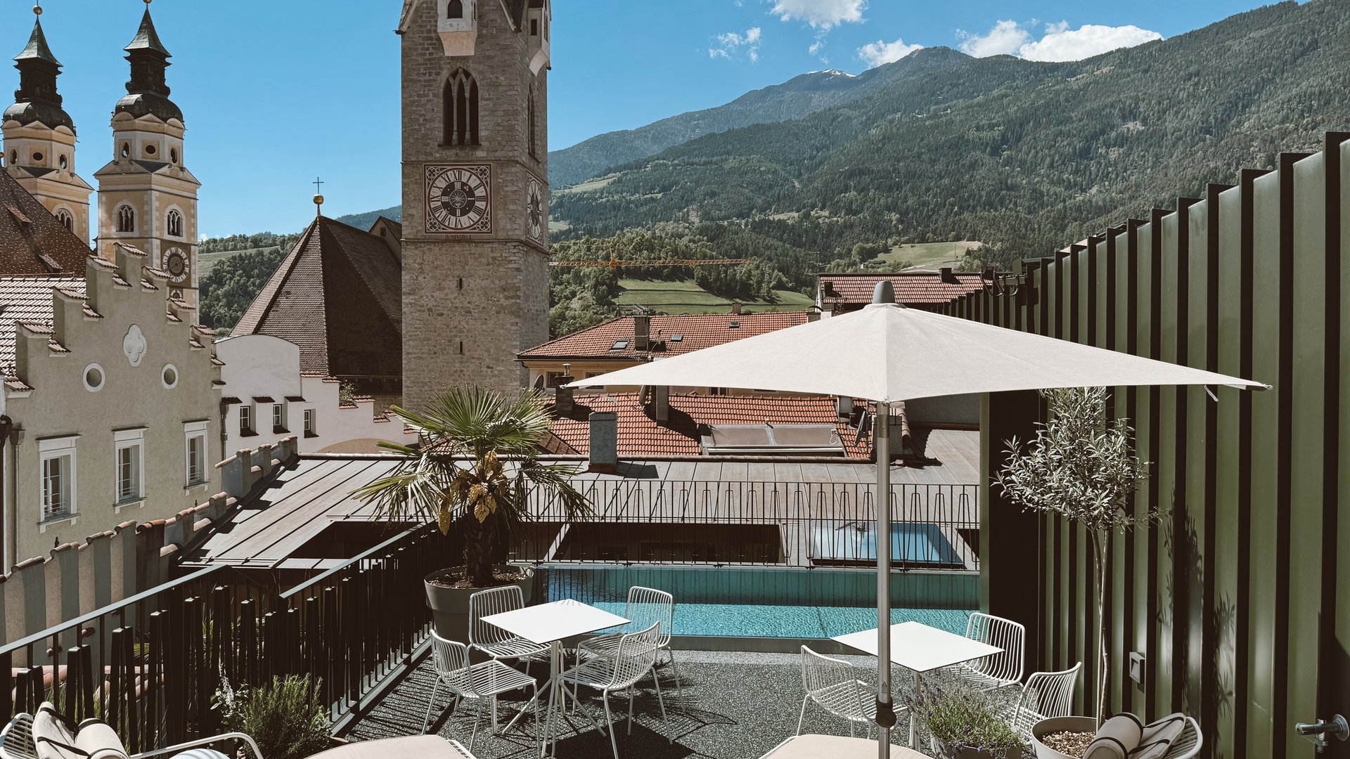 Dachterrasse mit Pool und Blick auf Kirchtürme und Berge bei klarem Himmel